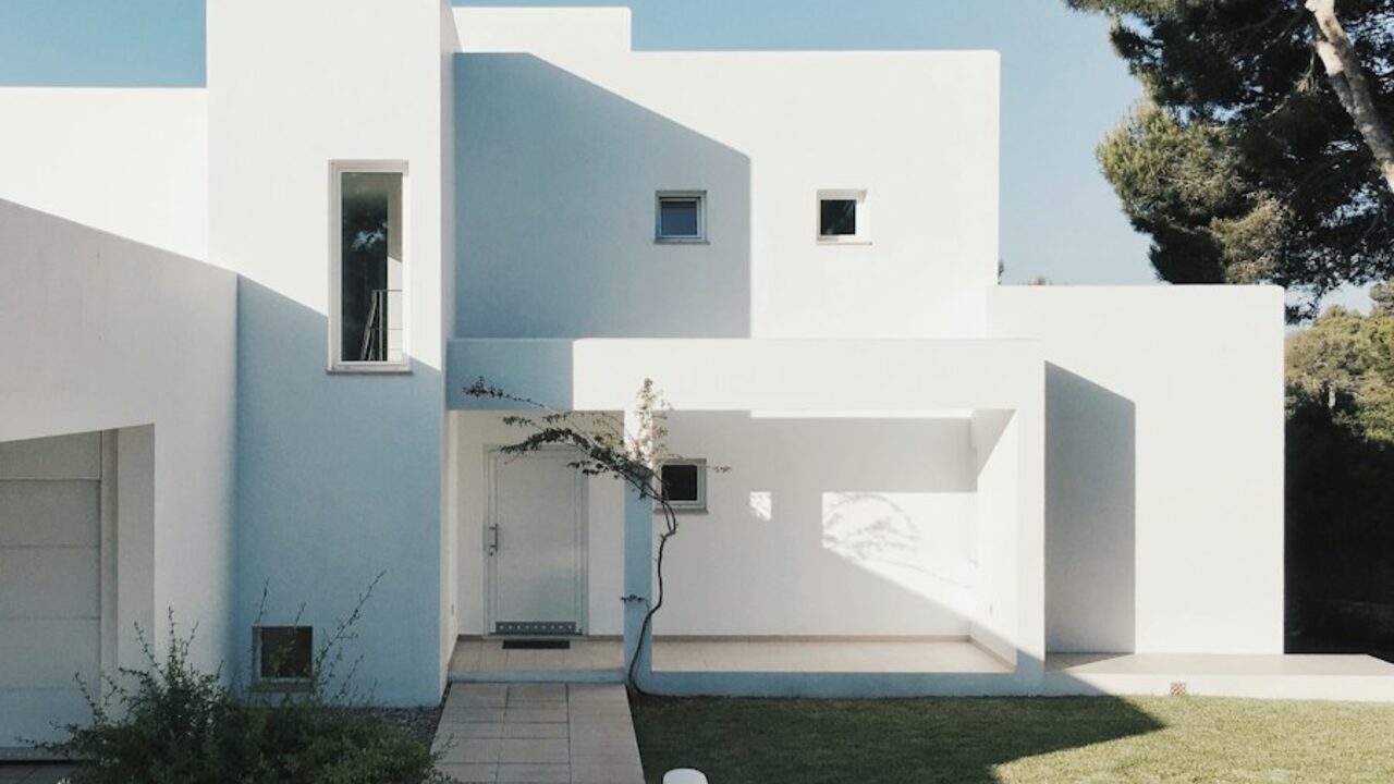 Concept visual: a minimalist white residence with clean volumes and a paved entrance.